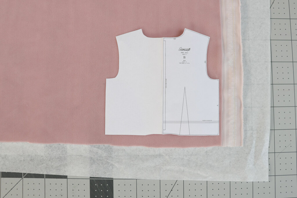 A pattern piece being cut out with tissue paper under velvet to stabilize it