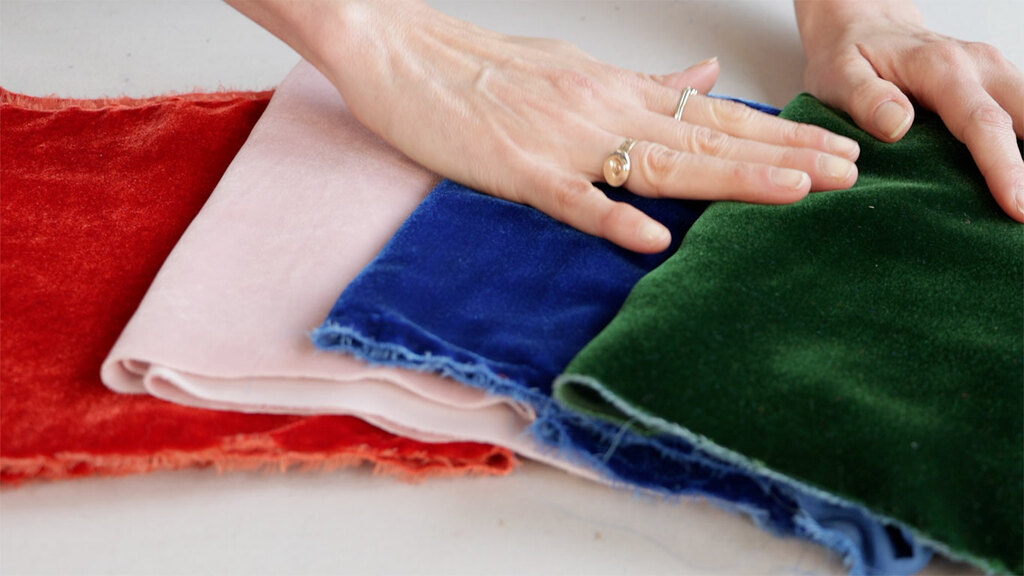 Sarai's hand petting a stack of velvet fabric in a bunch of colors