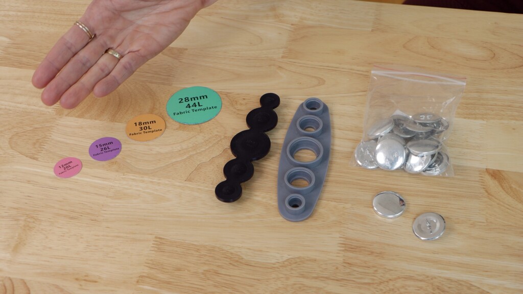 Covered button kit components laid out - front mold, back piece, pushing tool, and fabric templates